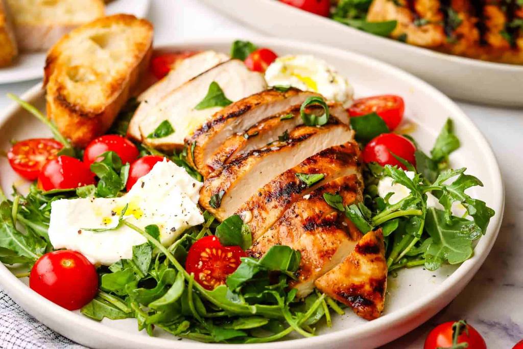 Fresh green salad with grilled chicken, tomatoes, and light vinaigrette dressing on a white plate.
