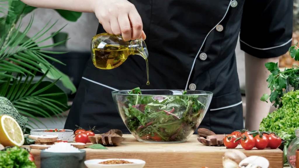 Person measuring olive oil for homemade salad dressing in a kitchen setting.
